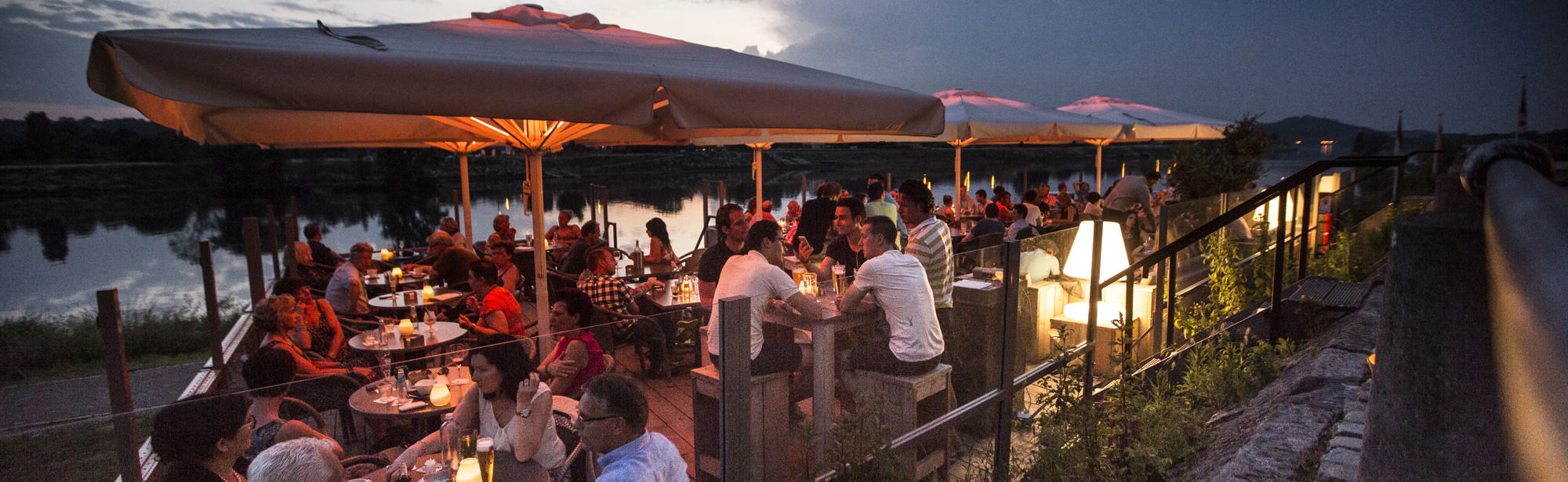 Een druk terras in de avond bij eetcafe Bat Eijsden aan de Maas