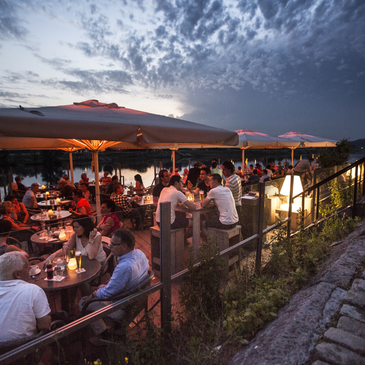 Mensen zitten onder de parasols op het terras van Eetcafé Aon 't Bat in Eijsden in de avond